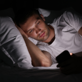 Man lying on bed in dark room looking at phone