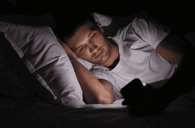 Man lying on bed in dark room looking at phone